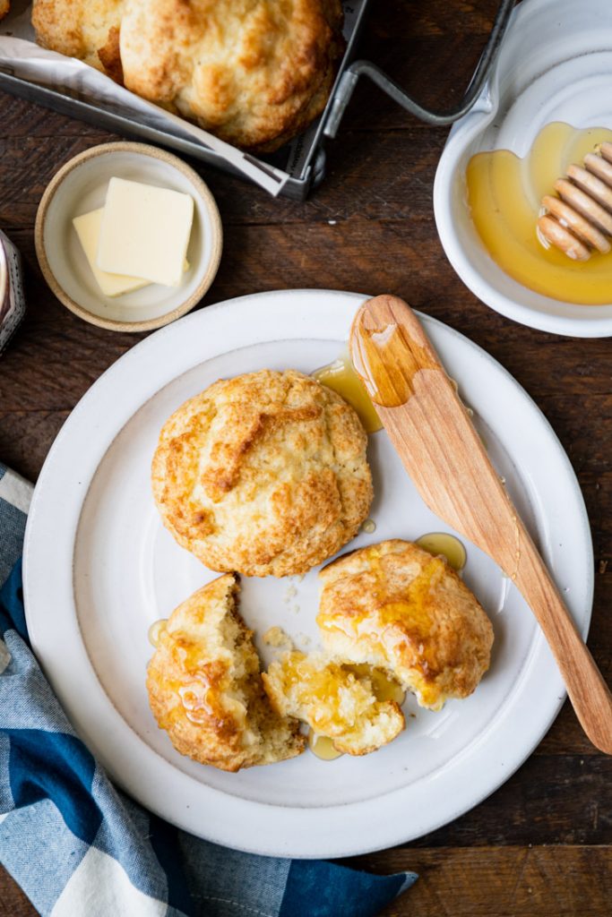 Overhead shot of drop biscuits on a white plate with honey and butter