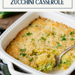 Side shot of a spoon in a white pan of zucchini casserole with text title box at top