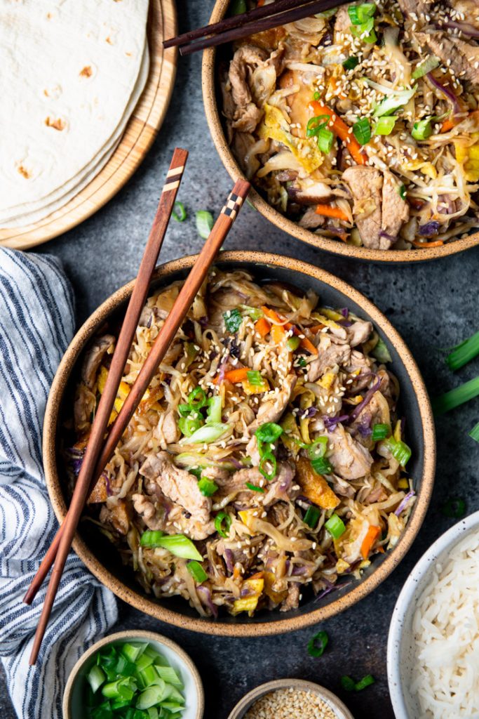 Overhead shot of two bowls of moo shu pork on a table with chopsticks