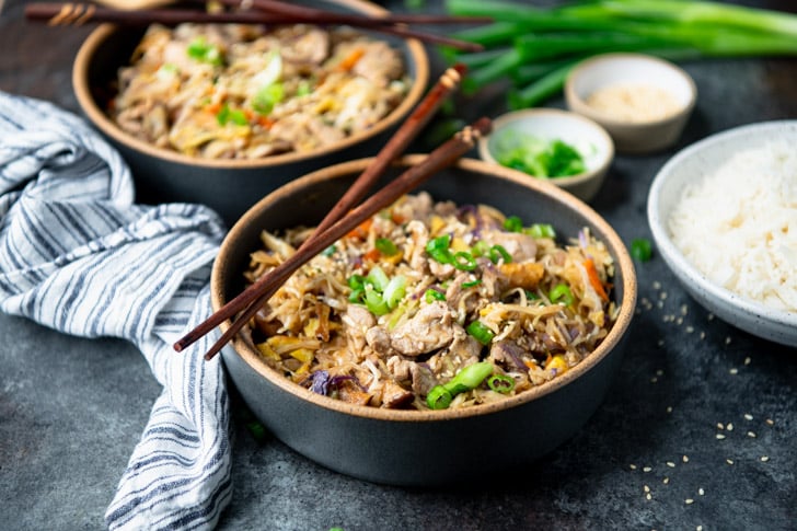 Close horizontal front shot of two bowls of moo shu pork on a dinner table.