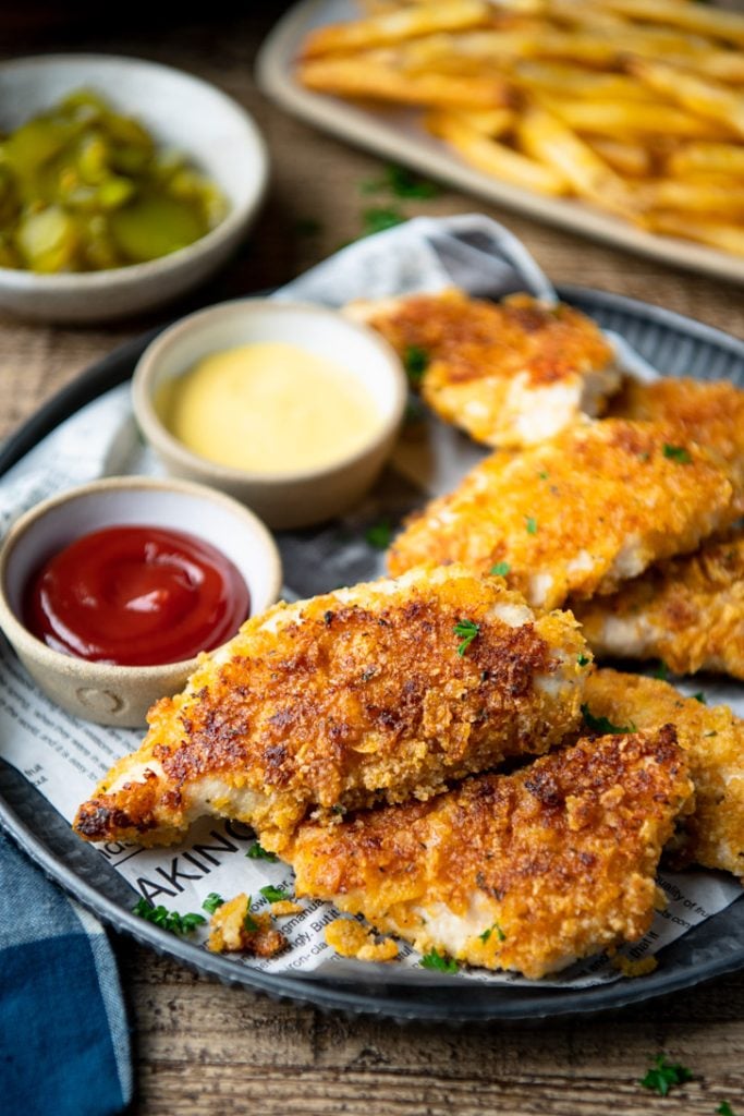 The best baked chicken tenders recipe on a plate with ketchup and honey mustard for dipping