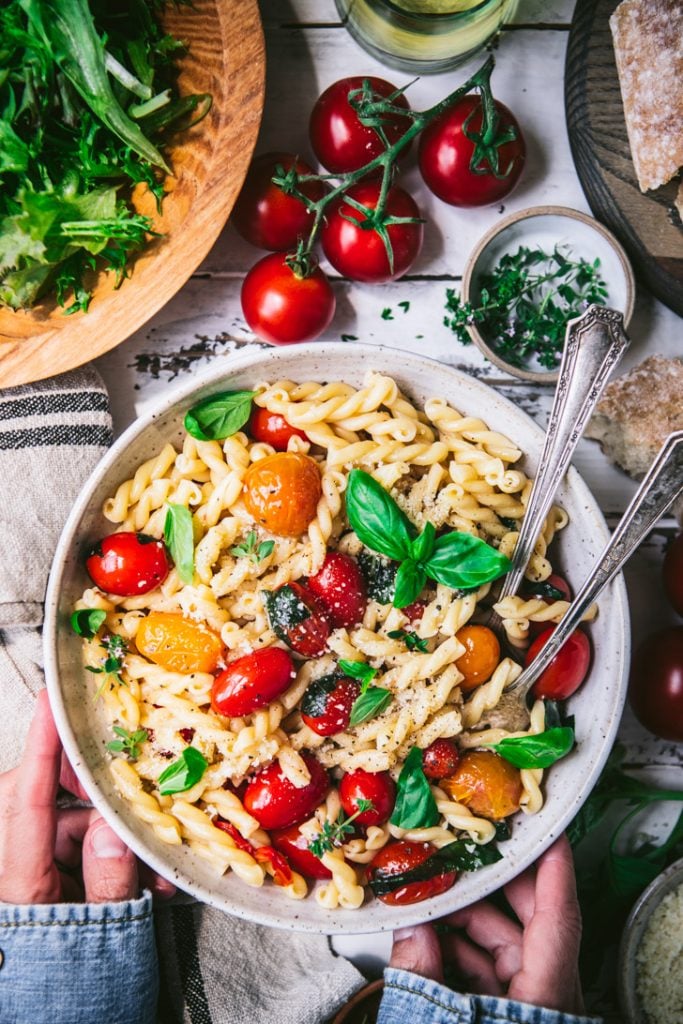 Overhead shot of hands holding a bowl of pasta with cherry tomatoes