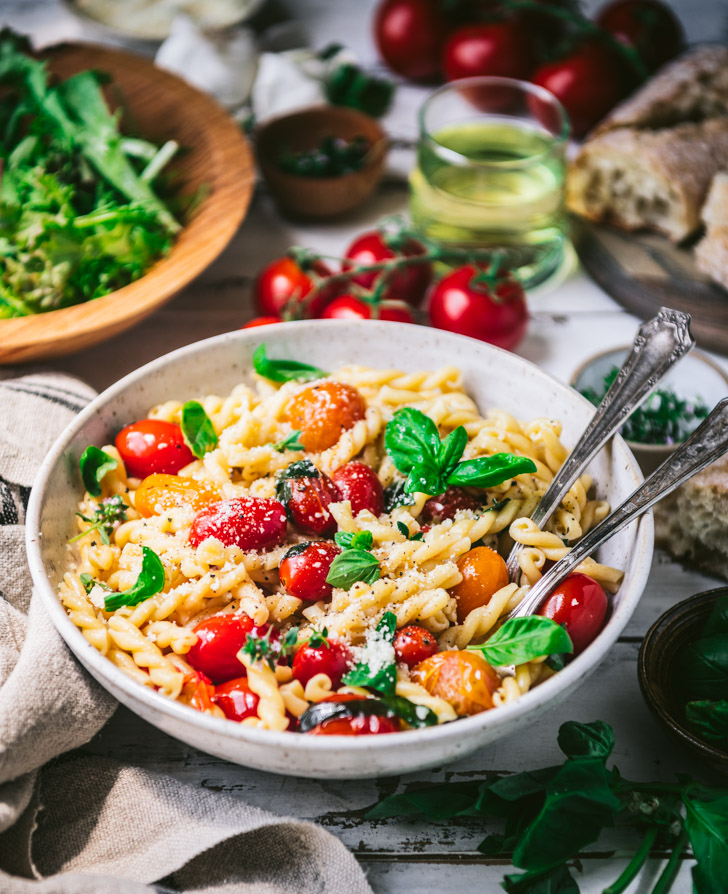 Side shot of a bowl of pasta with cherry tomatoes on a dinner table with a glass of wine