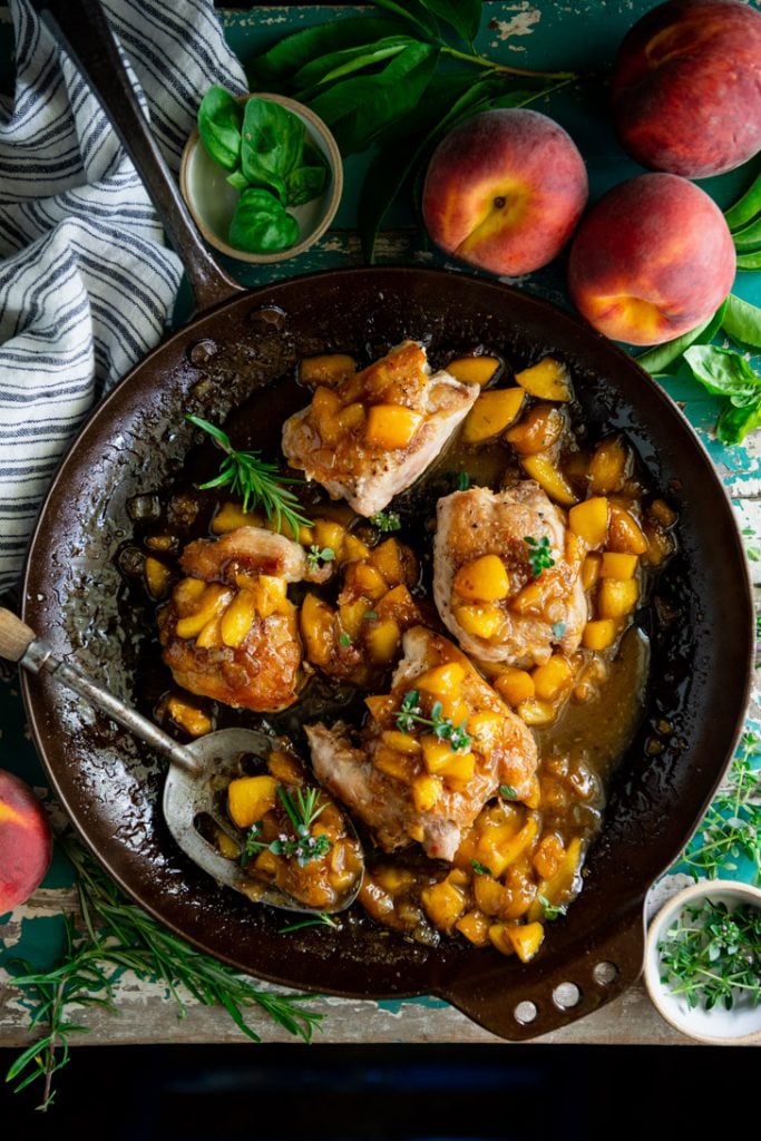 Overhead shot of a cast iron skillet full of peach chicken with fresh herbs