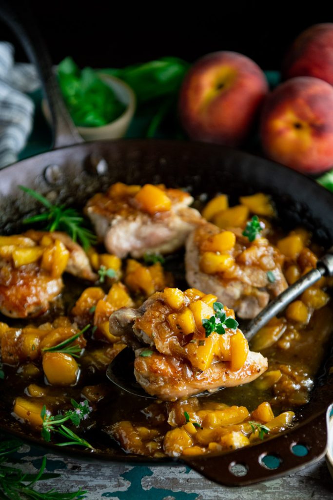 Side shot of peach chicken on a serving spoon in a skillet
