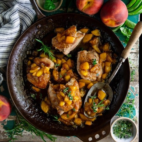 Large overhead featured square image of peach chicken thighs in a skillet