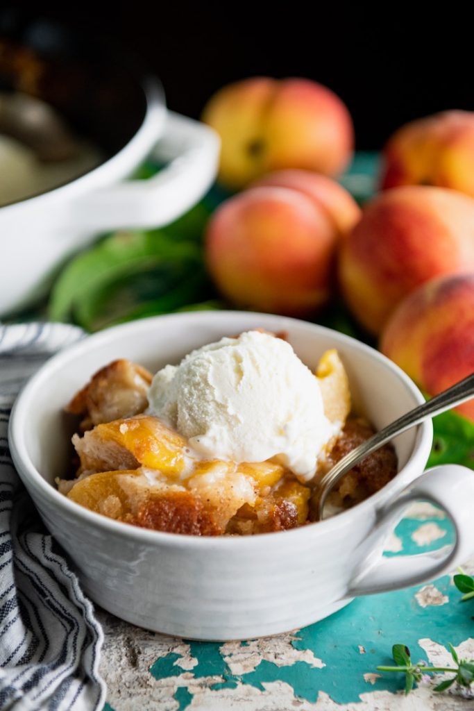 Side shot of a bowl of easy peach cobbler with vanilla ice cream on top