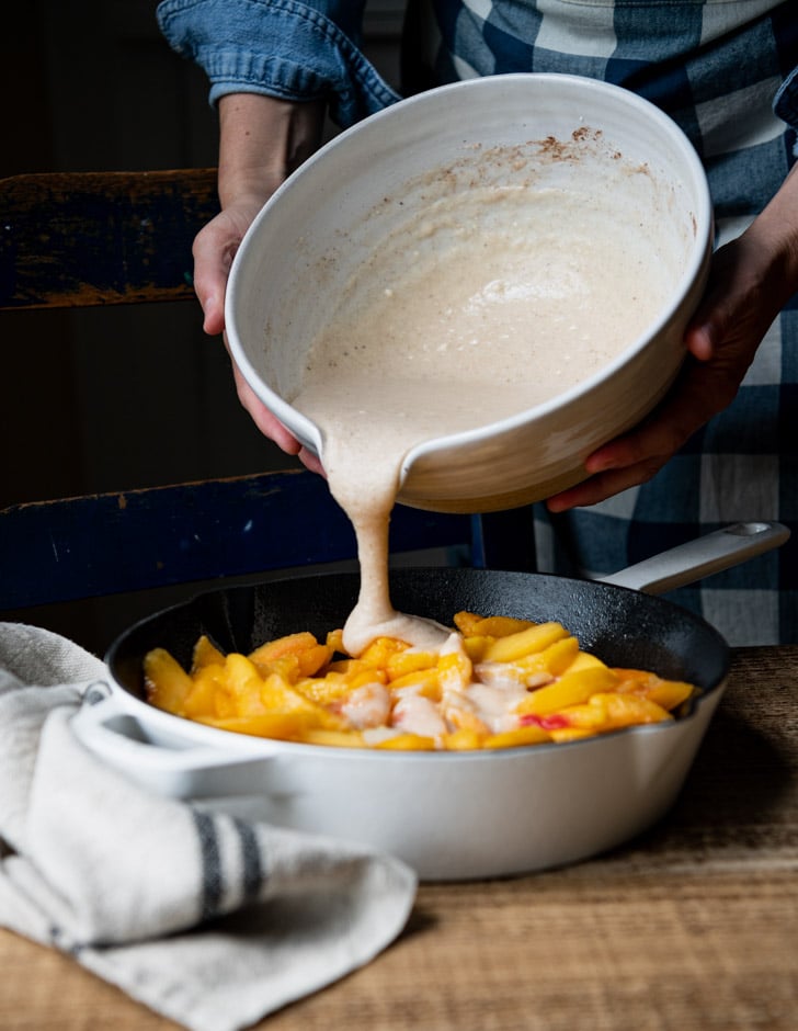 Pouring batter over skillet of peaches