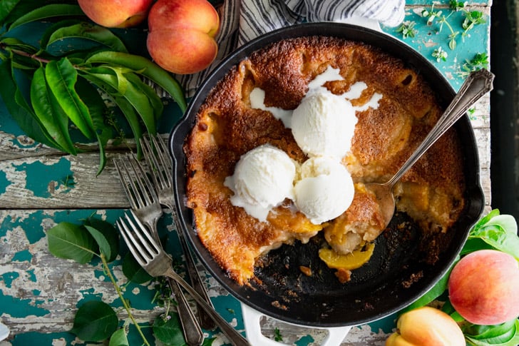 Horizontal overhead shot of a skillet of peach cobbler on an antique turquoise table