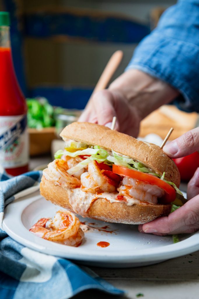 Hands picking up a homemade shrimp po boy from a plate