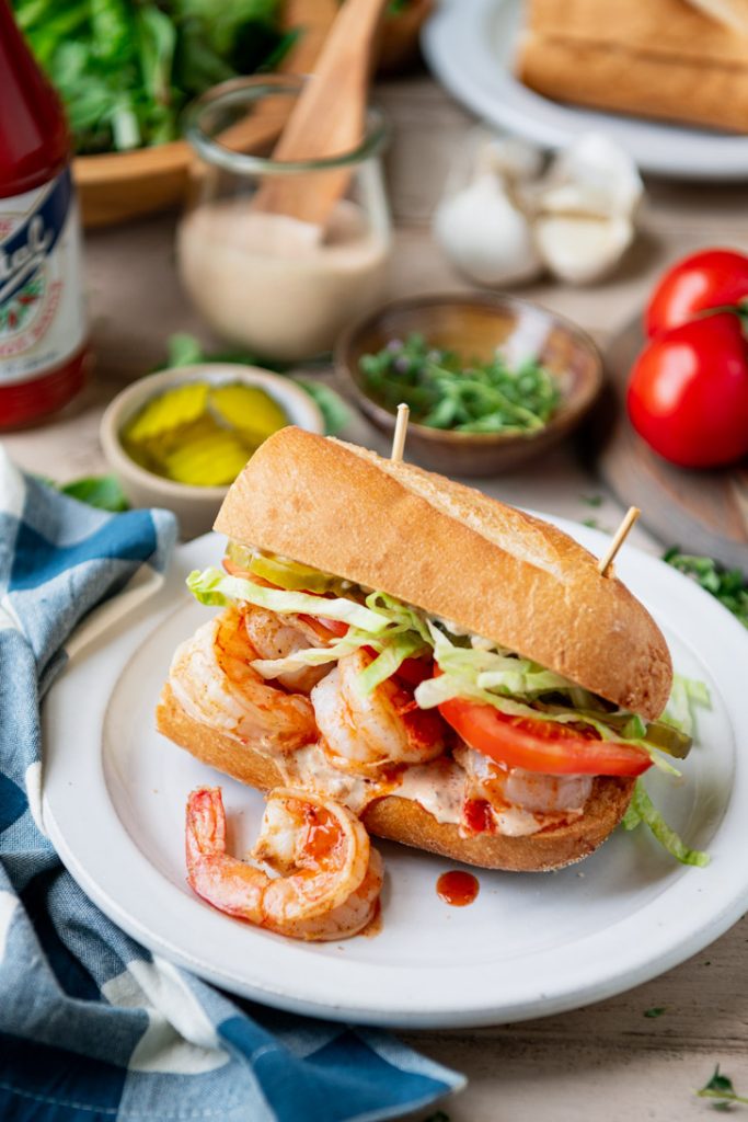Baked shrimp po boy recipe served on a white plate with pickles and remoulade sauce in the background