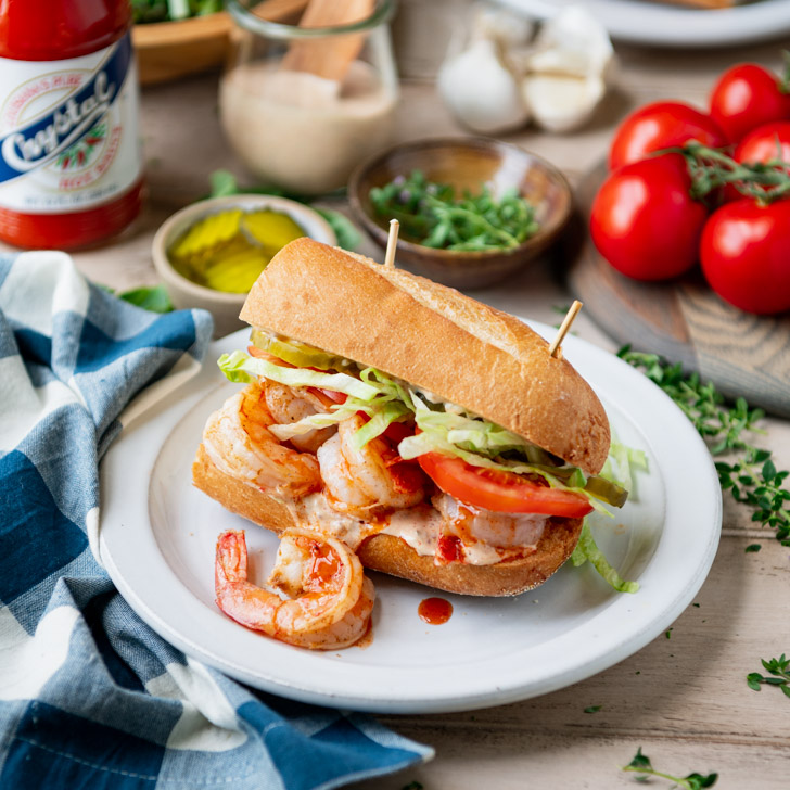 Square side shot of a shrimp po boy on a white plate with blue and white check napkins