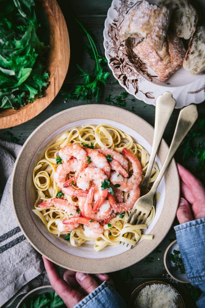 Overhead shot of hands holding a bowl of shrimp scampi pasta