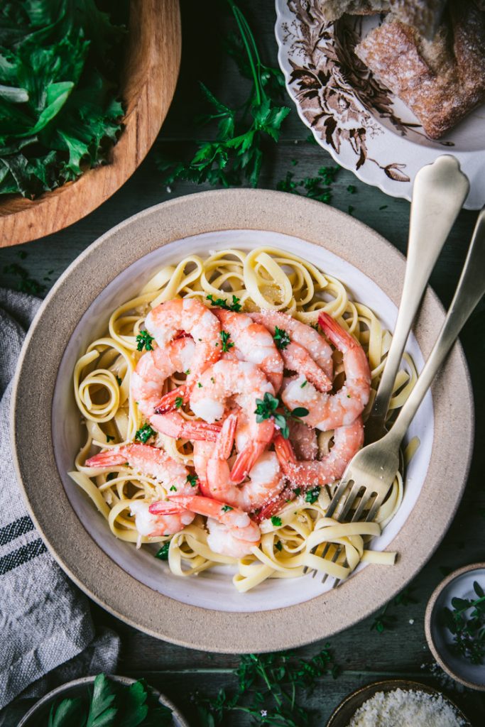 Gold utensils in a bowl of shrimp scampi with pasta
