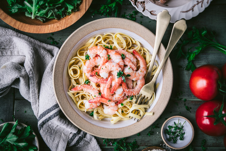 Horizontal overhead shot of a bowl of shrimp scampi on a wooden dinner table