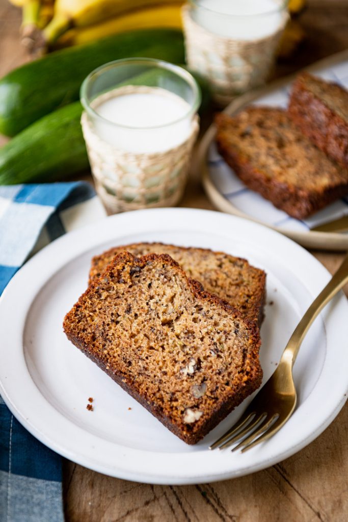 Two slices of zucchini banana nut bread on a white plate with a gold fork