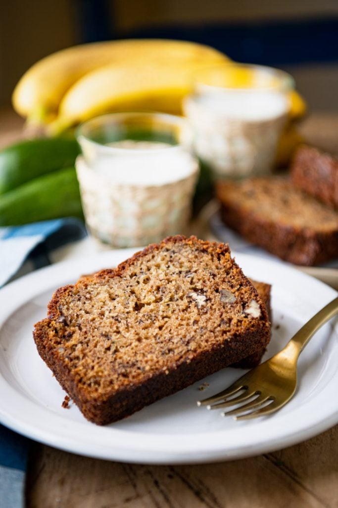 Side shot of slices of banana zucchini bread on a white plate with milk in the background