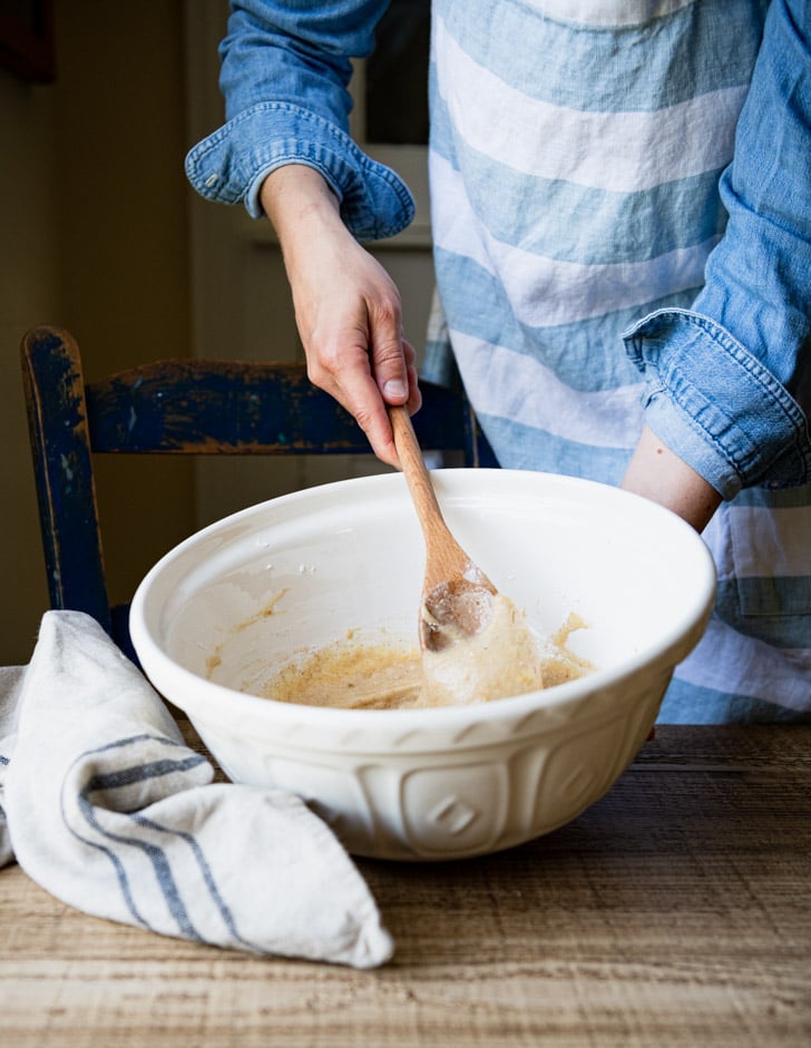 Stirring together zucchini banana bread batter in a white bowl with a wooden spoon