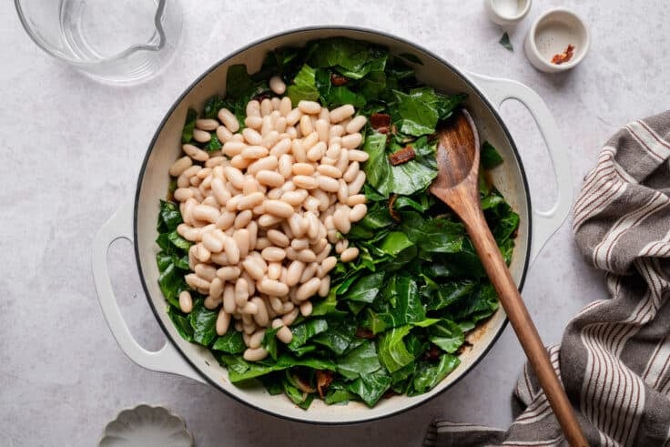 Adding the canned white beans to the skillet with the greens.