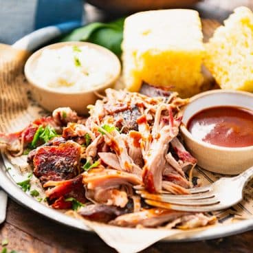 Square side shot of a plate of Mississippi pork shoulder roast recipe on a platter with cornbread and coleslaw.