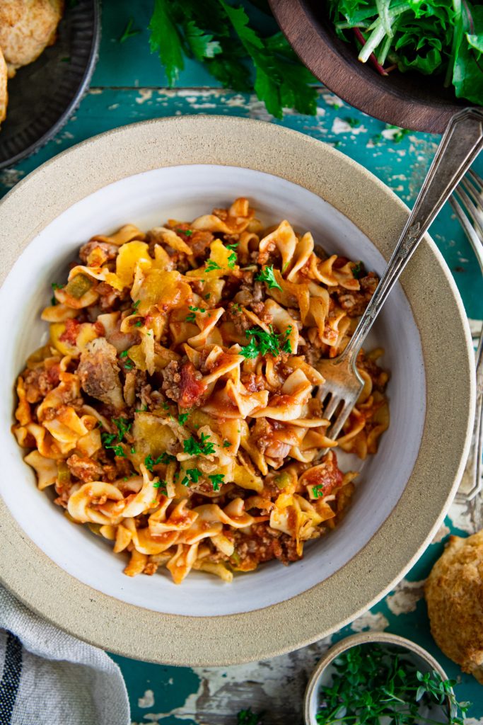 Close overhead image of a fork in a bowl of beef noodle casserole on a turquoise vintage table
