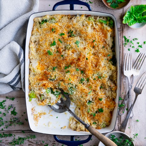 Overhead shot of a pan of broccoli cheese chicken and rice casserole on a wooden table with fresh herbs