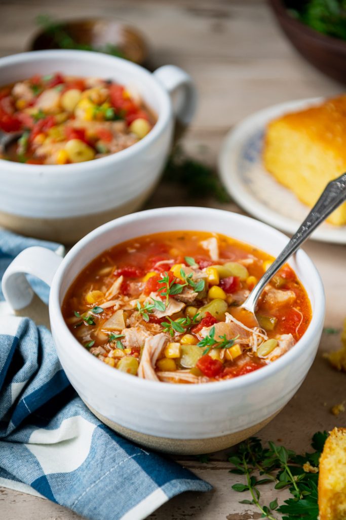 Side shot of two bowls of brunswick stew on a rustic table with cornbread