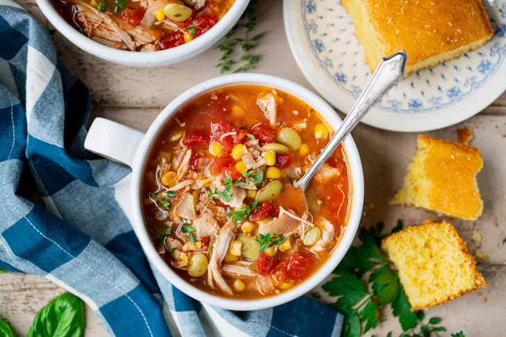 Horizontal overhead image of brunswick stew and cornbread on a light wooden table