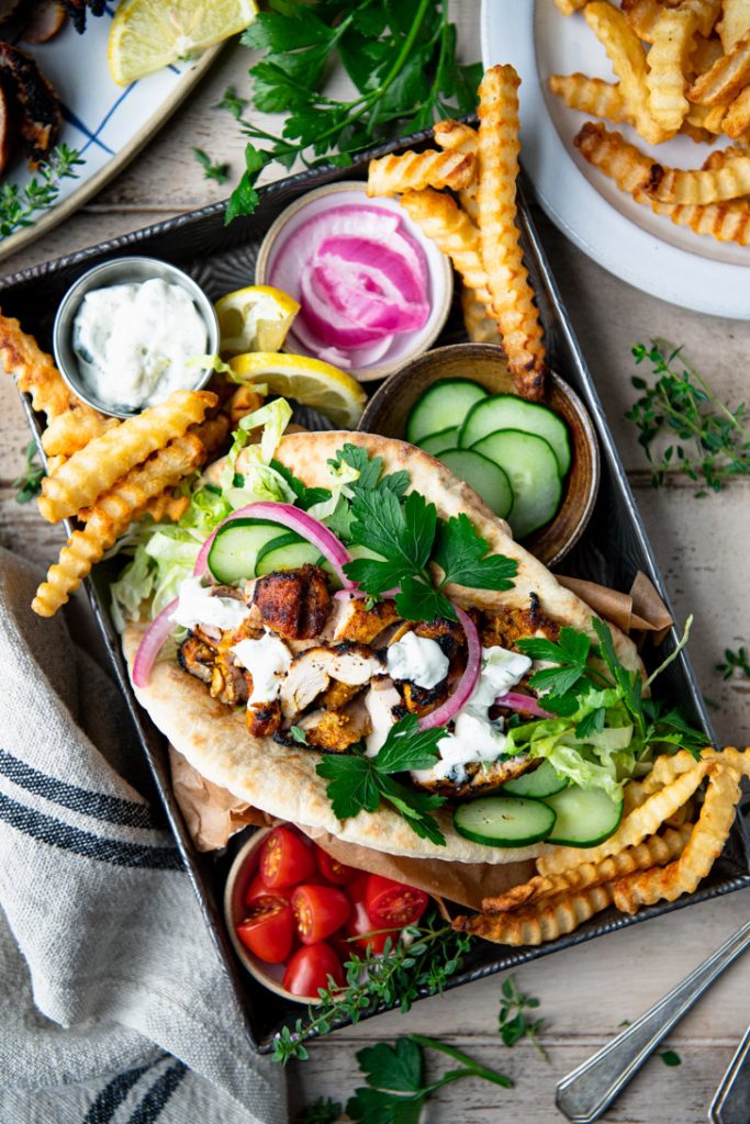 Close overhead shot of a chicken shawarma pita on a tray with yogurt sauce and veggies
