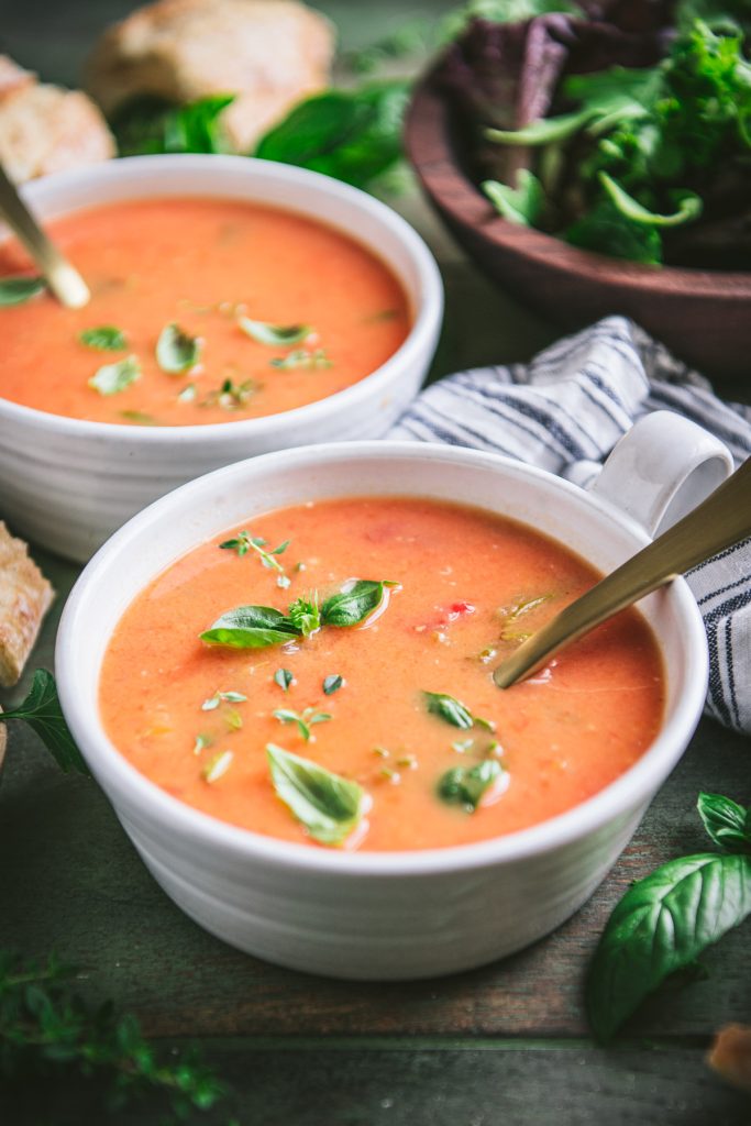 Close side shot of creamy tomato soup in white bowls on a green table