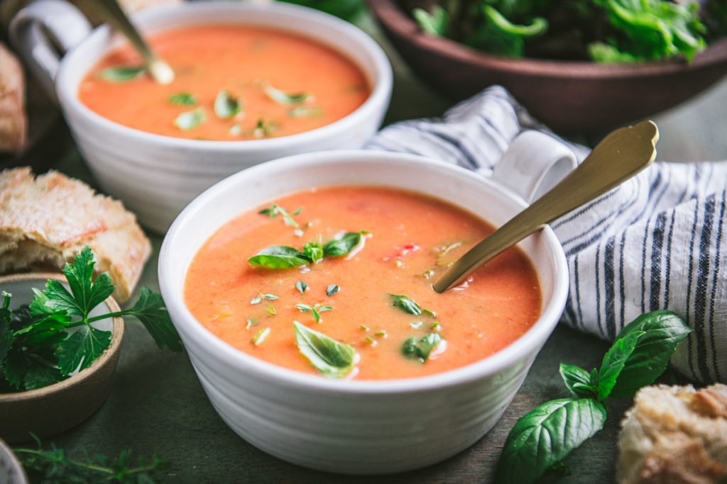Horizontal side shot of two bowls of roasted tomato soup on a green table