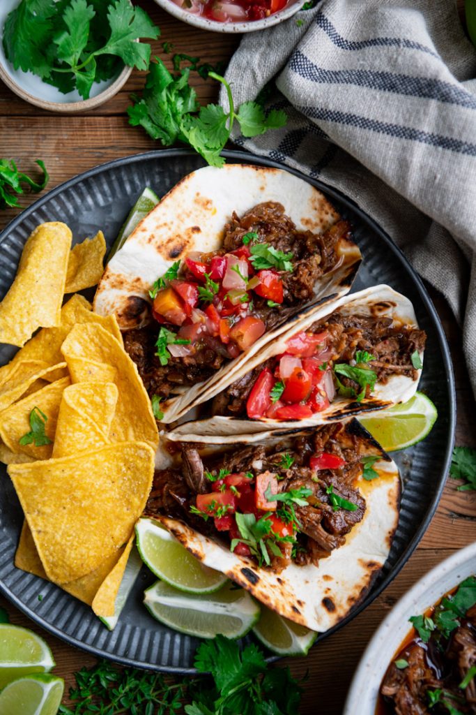 Close overhead image of shredded beef barbacoa soft tacos on a metal plate