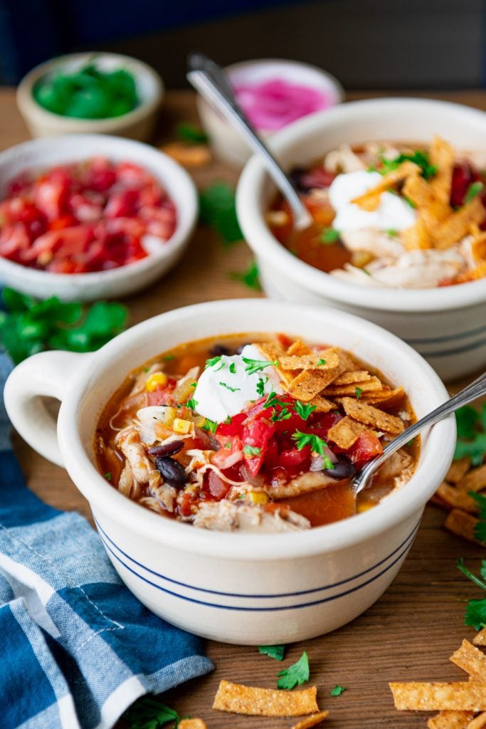 Side shot of a bowl of healthy chicken tortilla soup in a bowl on a wooden table