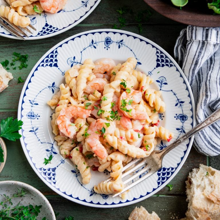 Square overhead shot of a plate of creamy shrimp pasta on a dinner table