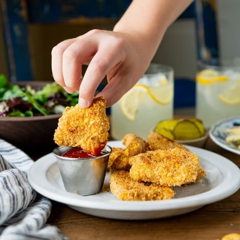 Child's hand dipping baked chicken nuggets in ketchup