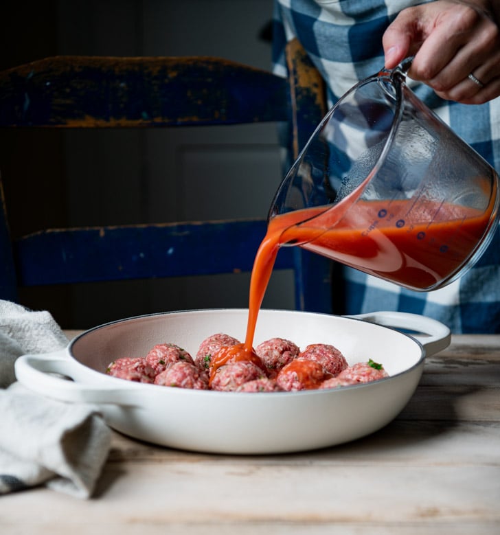 Pouring tomato soup mixture over meatballs