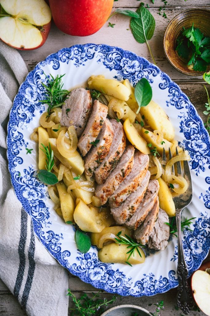Close overhead image of baked pork tenderloin with apples and onions served on a blue and white antique tray