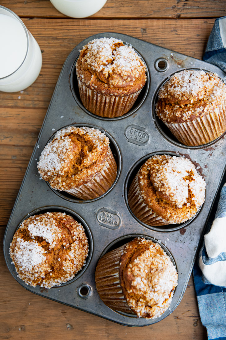 An overhead shot of six pumpkin muffins topped with crystal sugar sitting in a metal muffin tin.