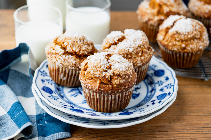 An image of three bakery style pumpkin muffins on a small plate, served alongside glasses of milk.
