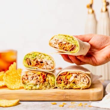 Hand picking up a bbq chicken wrap from a wooden cutting board.