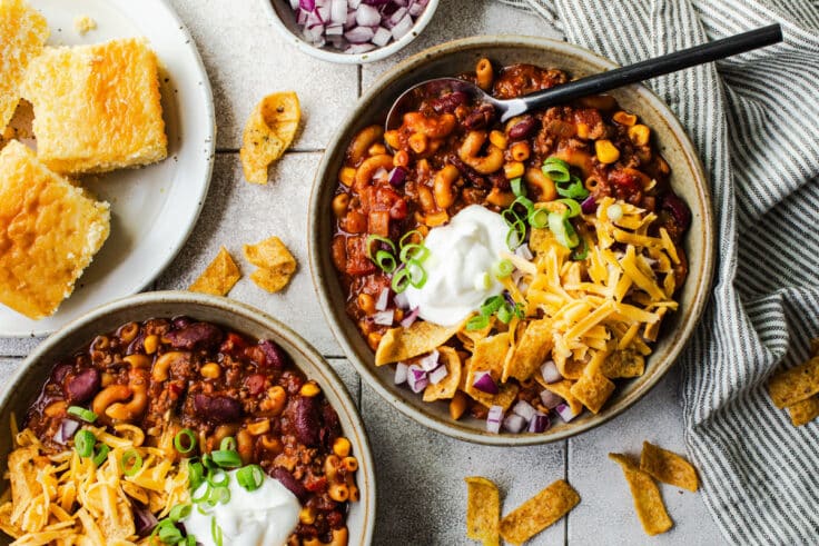 Horizontal overhead image of two bowls of chili mac with a side of cornbread.