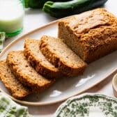 Horizontal side shot of a loaf of sliced zucchini bread on a white serving tray.