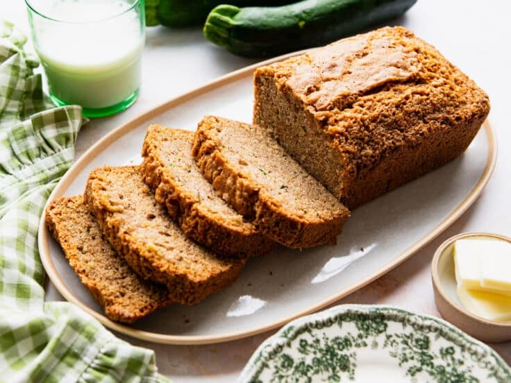 Horizontal side shot of a loaf of sliced zucchini bread on a white serving tray.