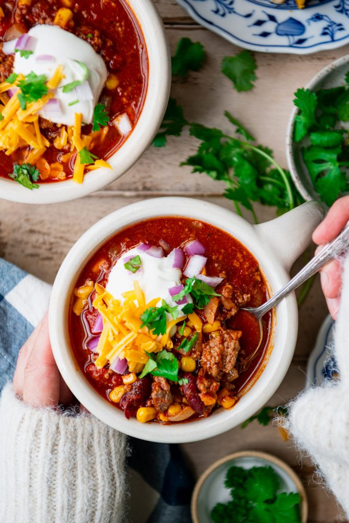 Overhead image of hands eating a bowl of beef and beer chili