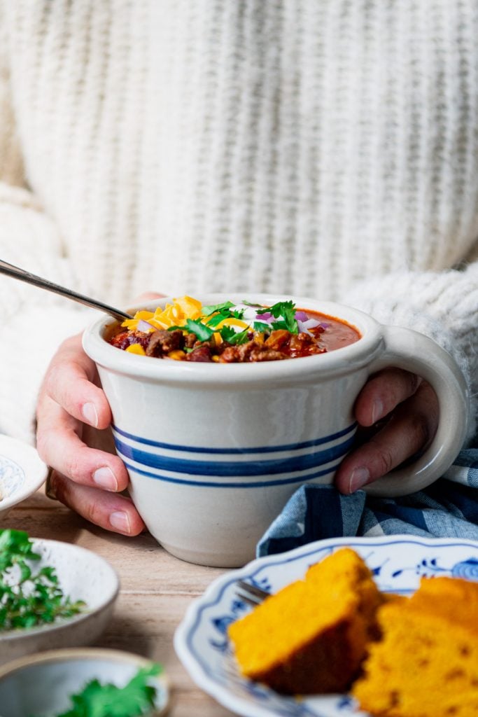 Front shot of hands holding a mug of beer chili with a white sweater