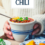 Front shot of hands holding a bowl of beer chili with text title overlay