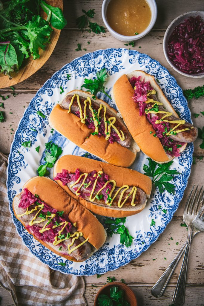Overhead shot of brats on sandwiches with red cabbage and mustard