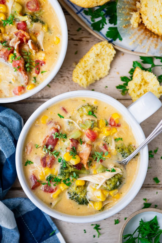 Overhead image of a bowl of cheesy chicken corn chowder on a dinner table with corn muffins