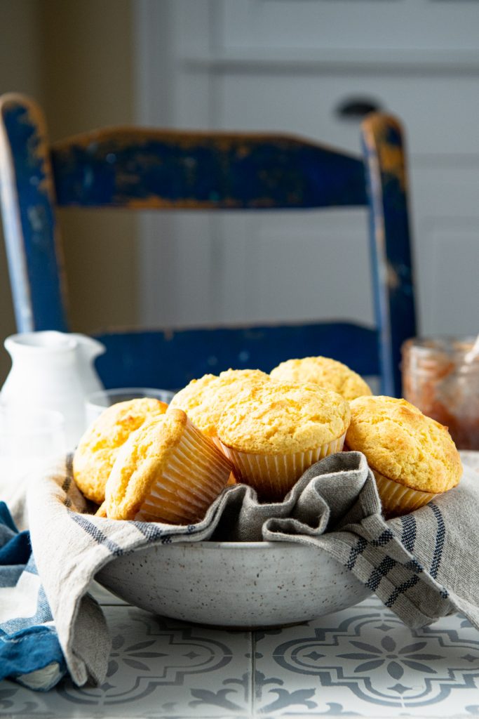 Side shot of a bowl of cornbread muffins on a table with apple butter