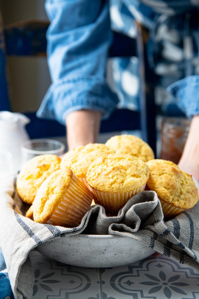 Hands serving a bowl of cornbread muffins on a table